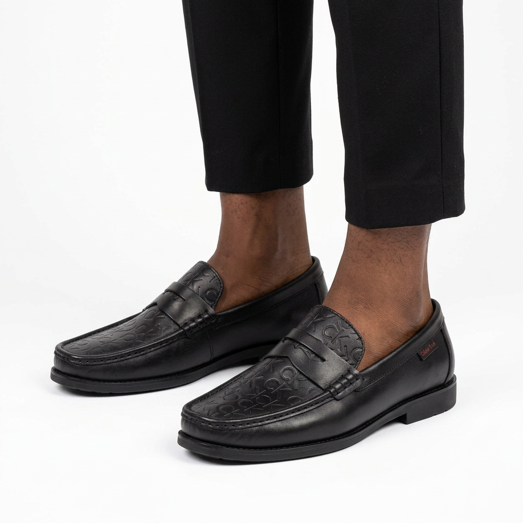Male model wearing black embossed penny loafers with both shoes visible on white