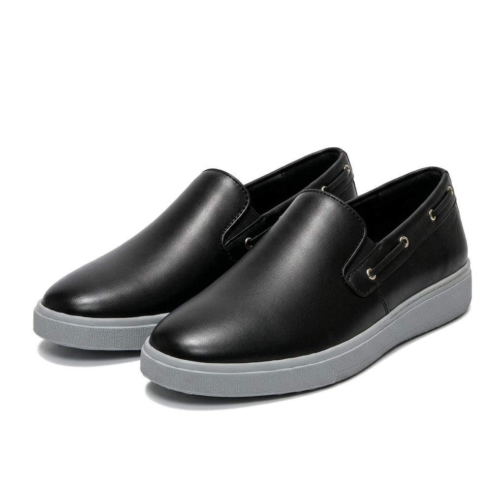 Matching pair of black slip-on shoes with grey soles and side eyelets on white
