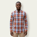 Male model wearing an orange and navy plaid long-sleeve shirt against a plain off-white background