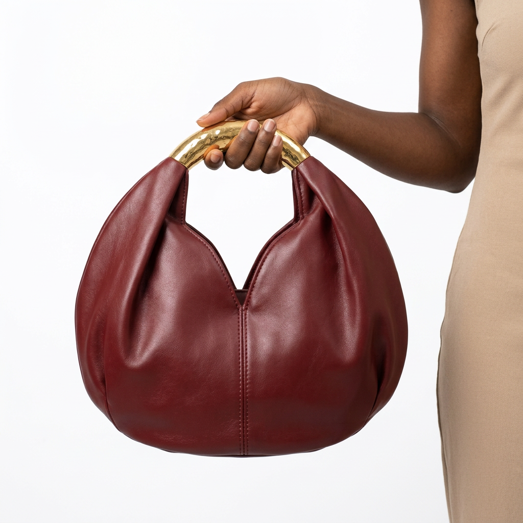 Wine-burgundy rounded handbag held by one hand gripping its gold-tone handle
