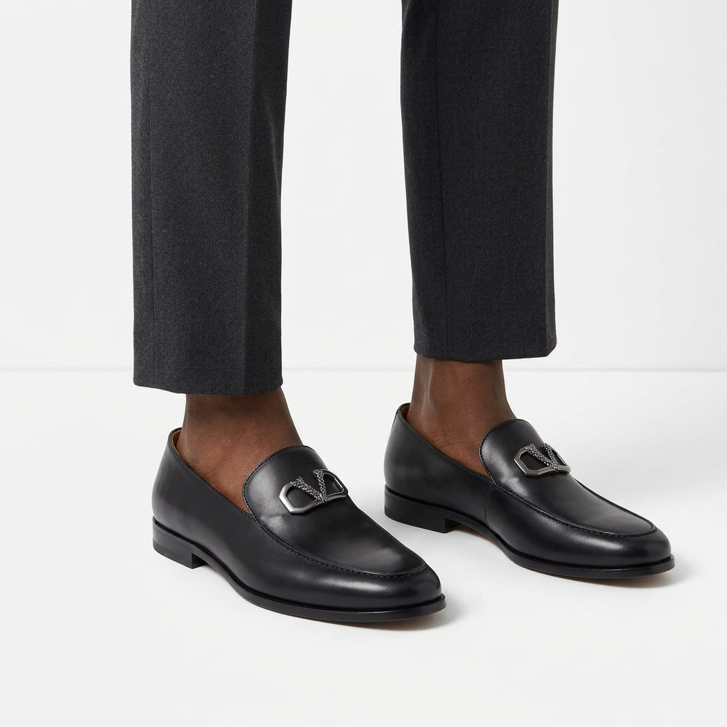 Black male model wearing both smooth black silver-detail loafers on white