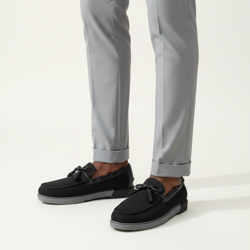 Black perforated suede boat shoes with grey sole worn with light grey trousers