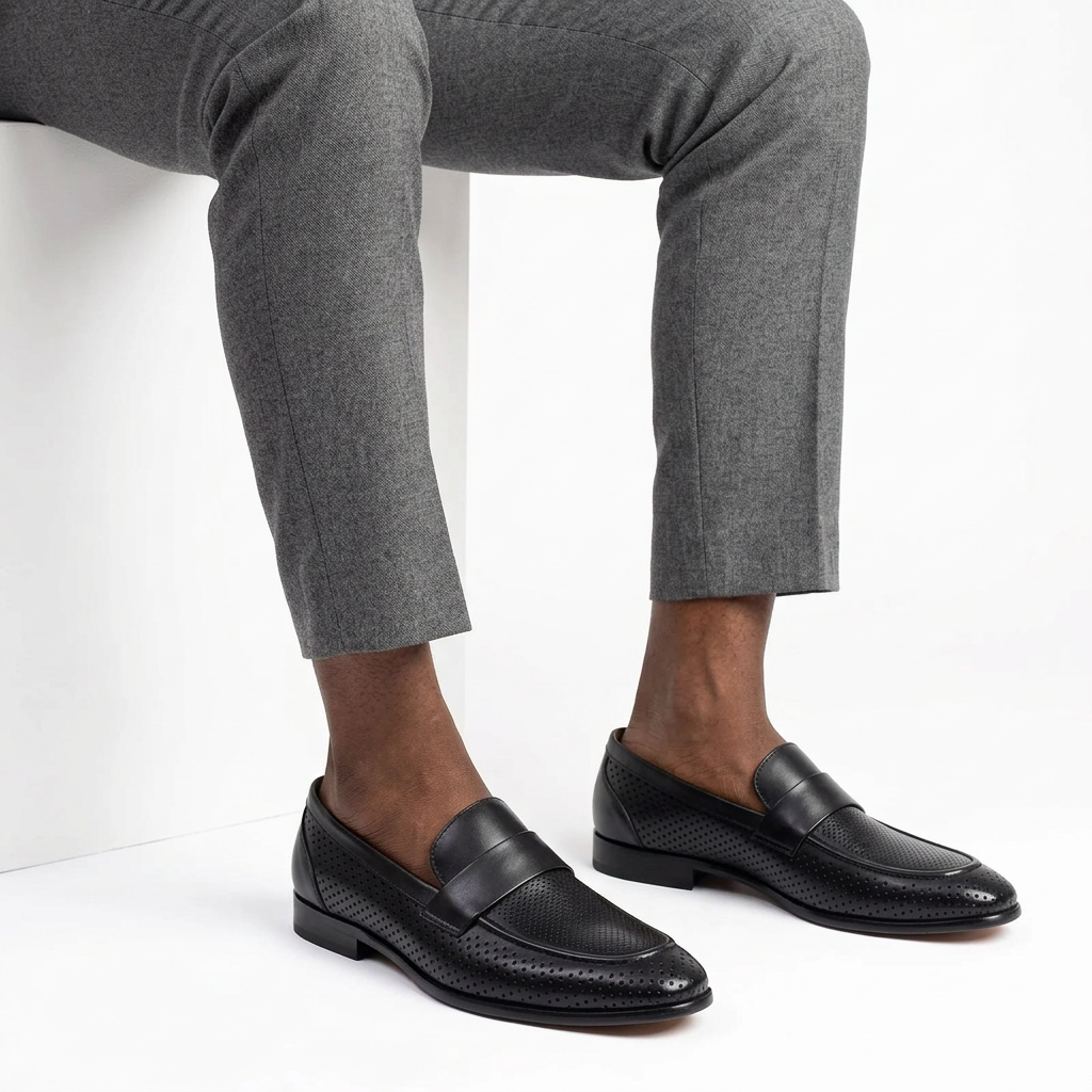 Black perforated strap loafers worn on both feet with grey trousers