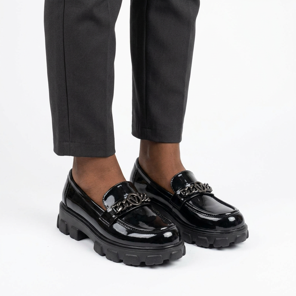 Adult woman wearing black glossy chain-accent loafers with feet together