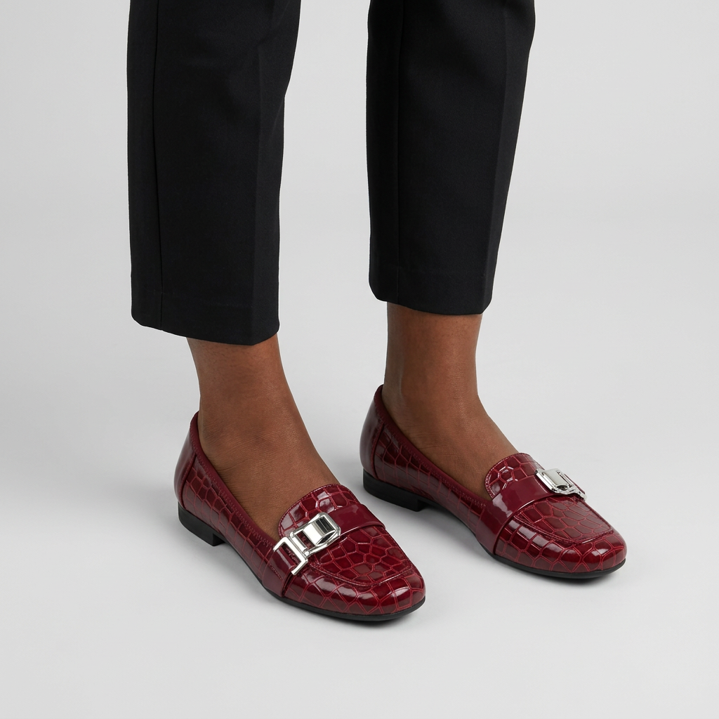 Woman wearing burgundy croc-texture buckle loafer flats on a plain studio background