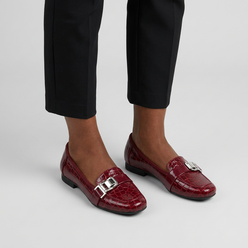 Woman wearing burgundy croc-texture buckle loafer flats on a plain studio background