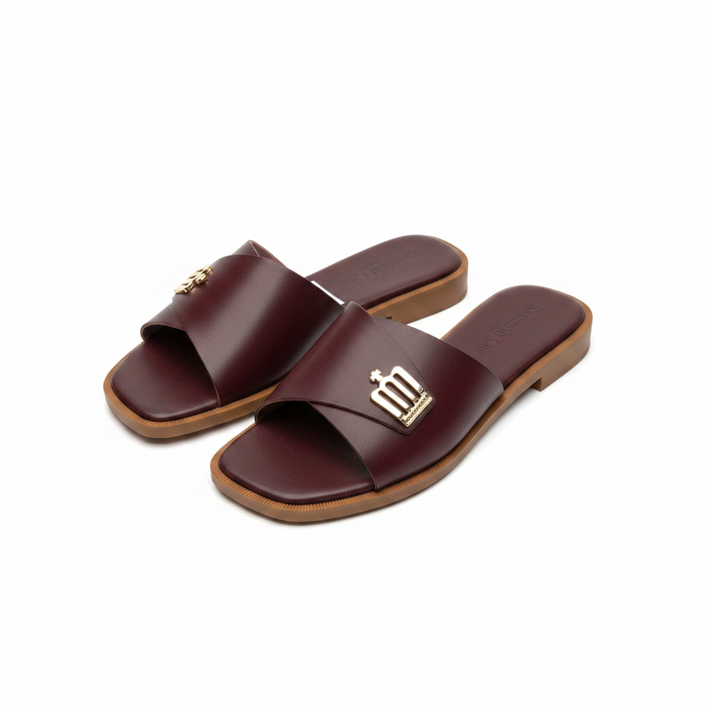 Pair of burgundy leather wide strap flat slide slippers with gold logo hardware on white background