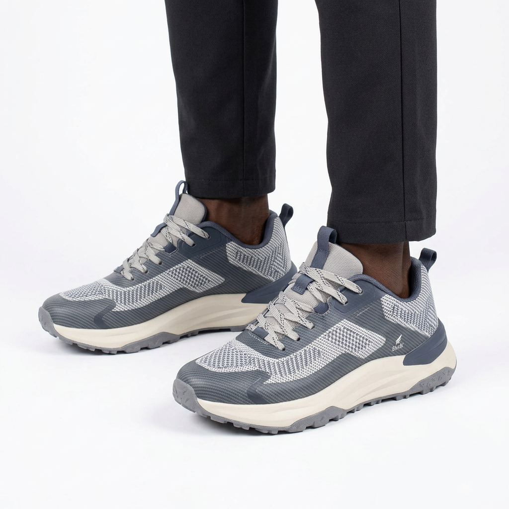 Black male model wearing both grey knit-panel sneakers on a white background