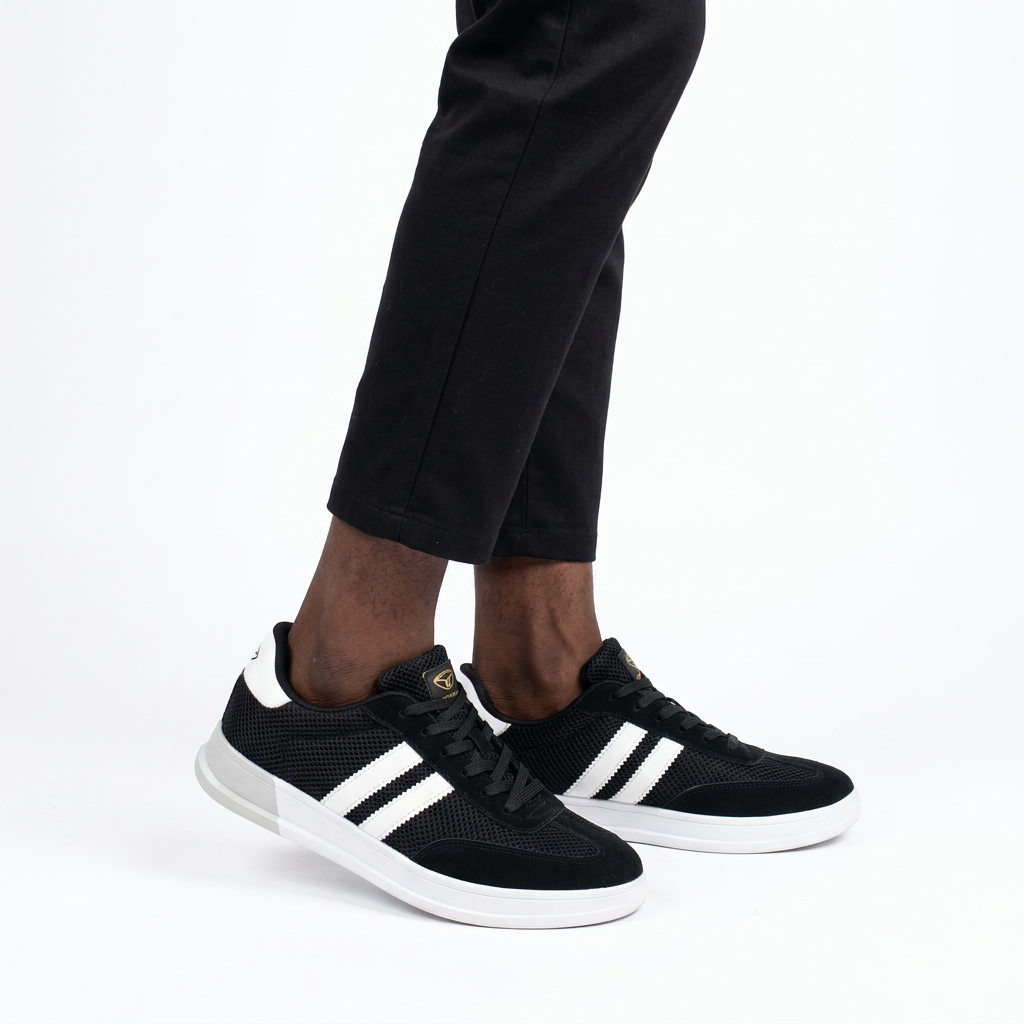 Black mesh sneakers with twin white stripes worn on both feet by a Black male model on a white background