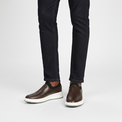 Man wearing brown leather slip-on sneakers with dark indigo jeans