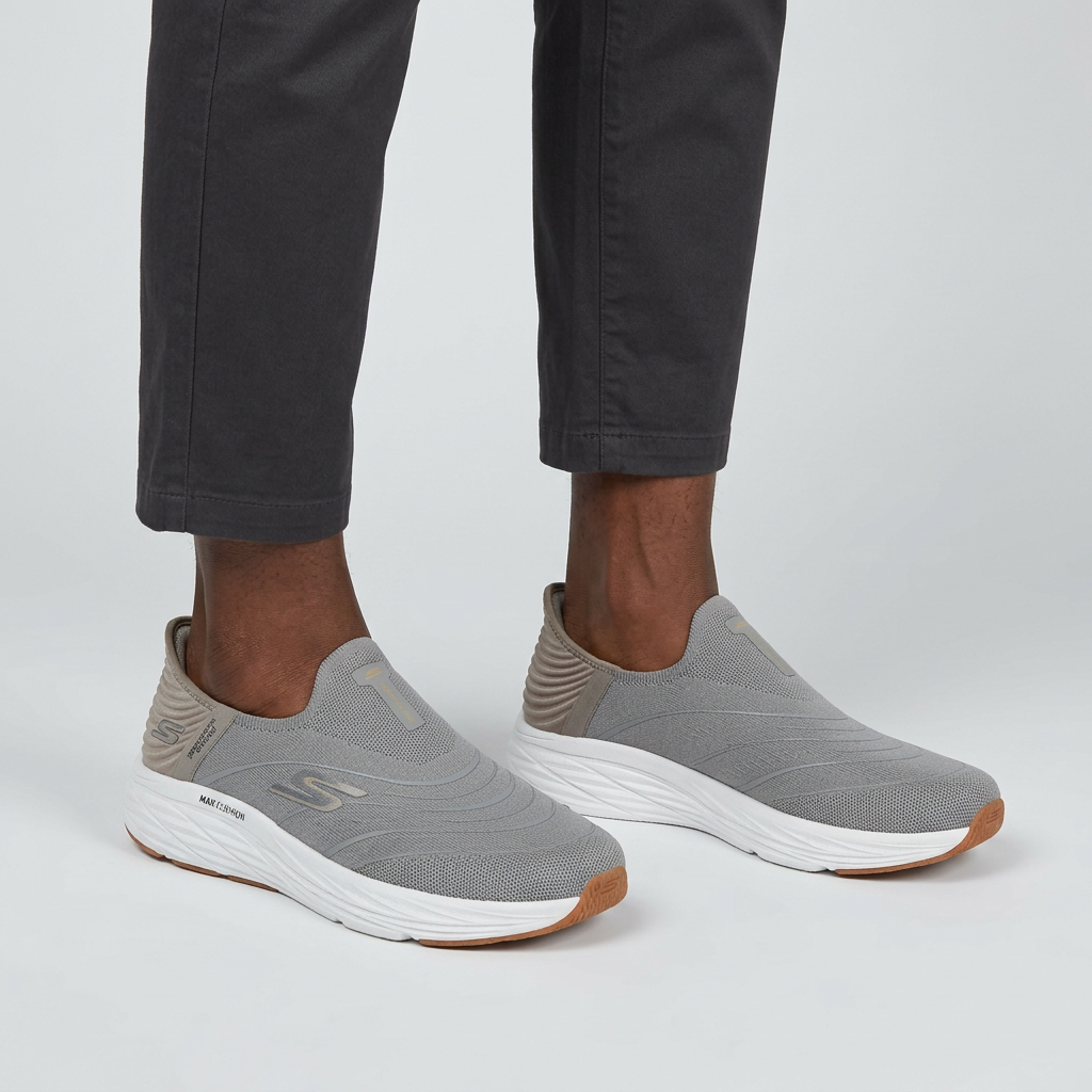 Grey mesh slip-on sneakers worn on both feet by a Black male model against a plain light-grey studio background