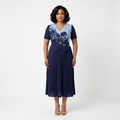 Black woman wearing navy floral-panel pleated midi dress on plain white background