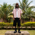 Nigerian male model full body wearing men's pink coral pinstripe boxy short-sleeve shirt open over white tee