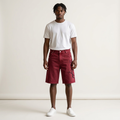 Male model wearing washed burgundy script denim shorts, a white tee and white trainers against a plain off-white background