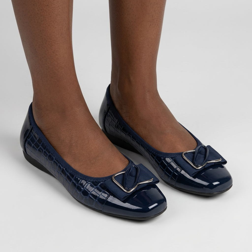 Woman wearing both navy croc-effect bow flats on plain studio background