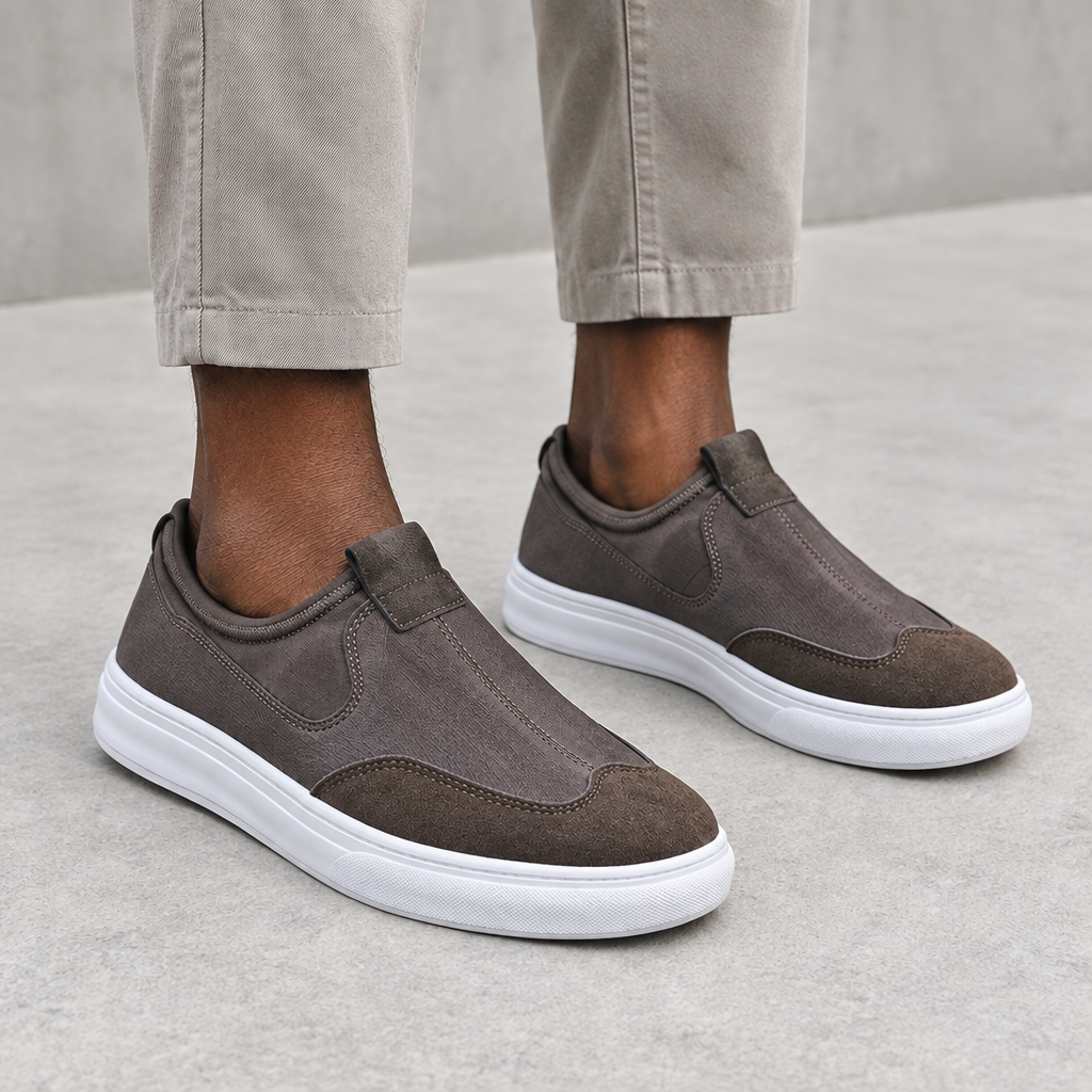 Men's grey and taupe slip-on sneakers with white soles worn on both feet