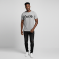 Young Nigerian male wearing light heather grey Our City script graphic crew neck tee