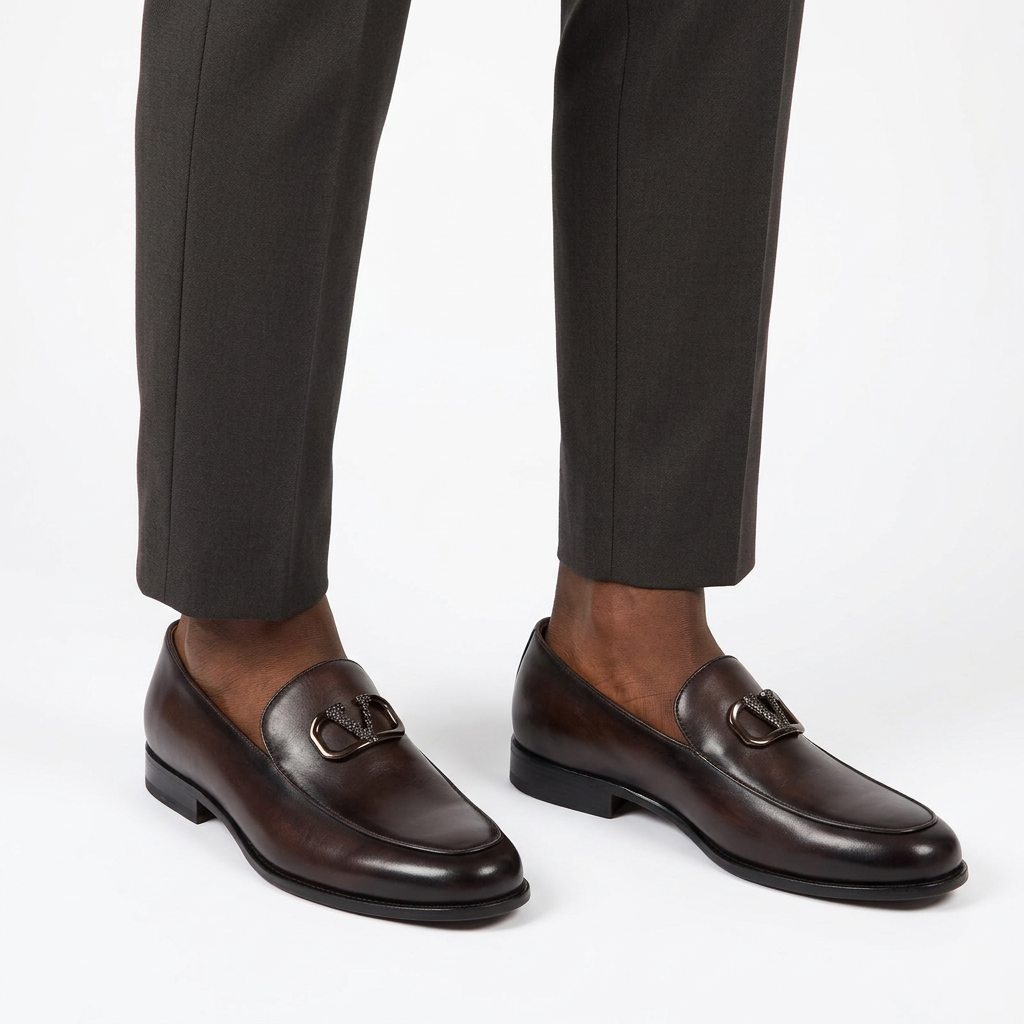 Black male model wearing both espresso-brown metal-detail loafers on white