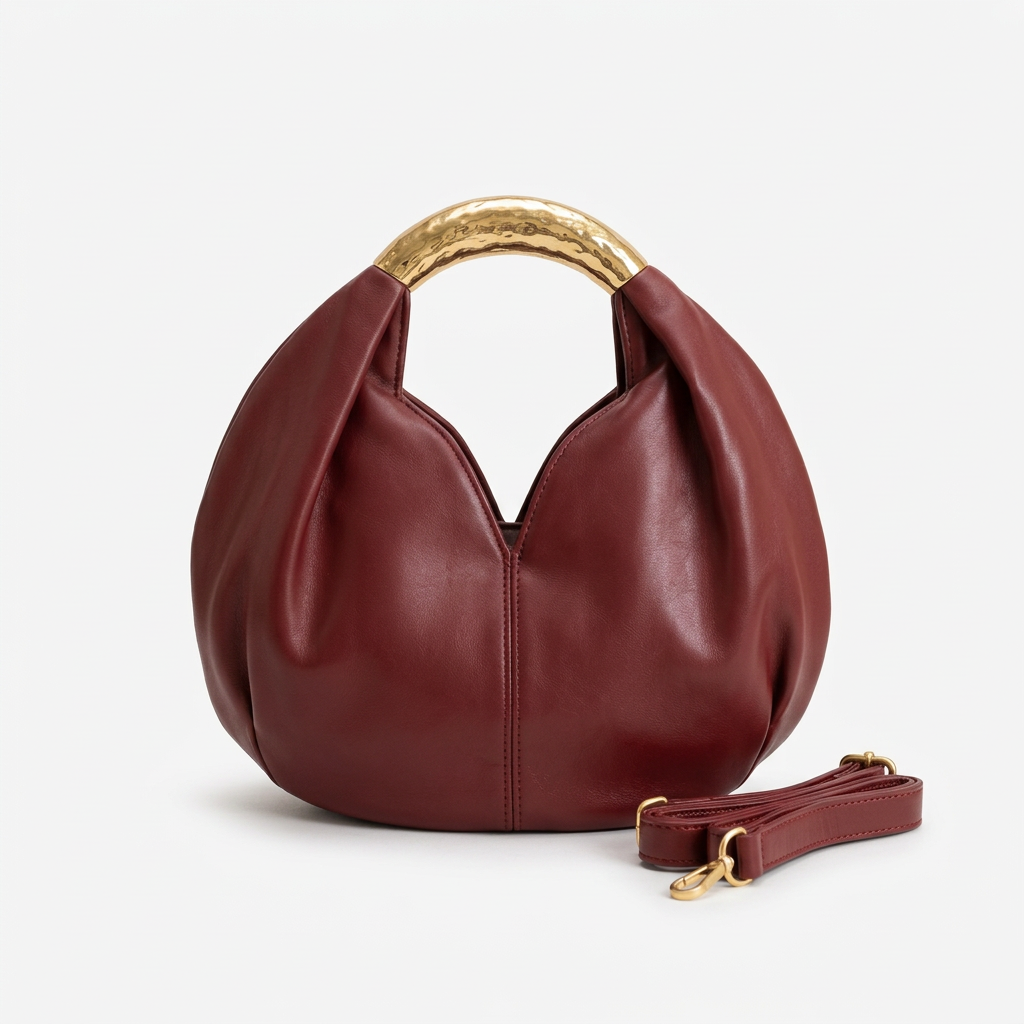Wine-burgundy rounded handbag with gold-tone handle and matching strap on white background