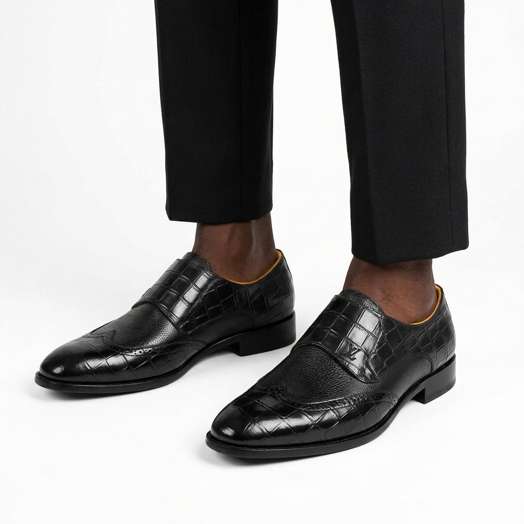 Black male model wearing both black croc-panel wingtip slip-ons on white