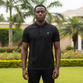 Nigerian male model wearing men's black polo shirt with tonal shoulder panel, garden setting