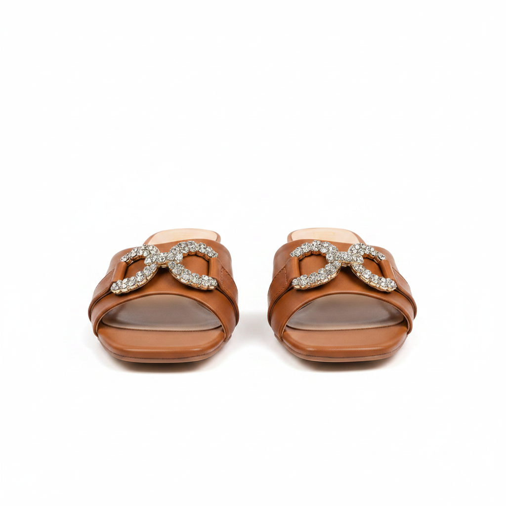 Pair of tan brown square-toe low block heel mule sandals with crystal buckle on white background