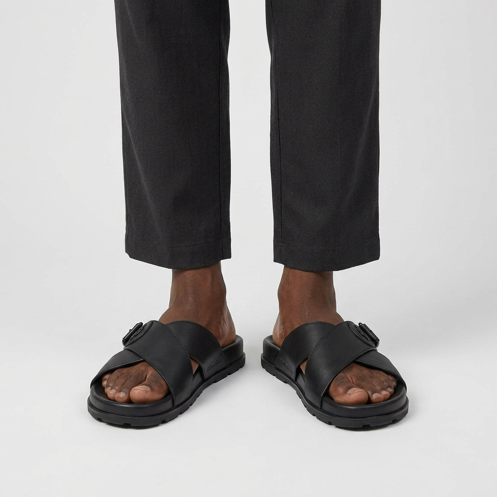 Man wearing black cross-strap slide slippers with buckle detail on a plain studio background
