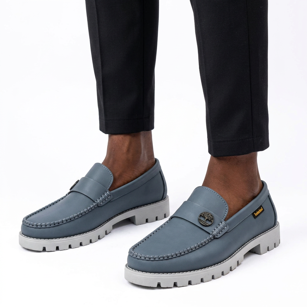 Male model wearing slate-grey emblem lug-sole loafers with both shoes visible on white