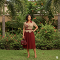 Nigerian female model wearing beige and burgundy two-tone pleated midi gown in upscale garden setting