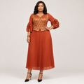 Black Nigerian model wearing a rust-orange pleated gown with a patterned bodice and floral cuff accents