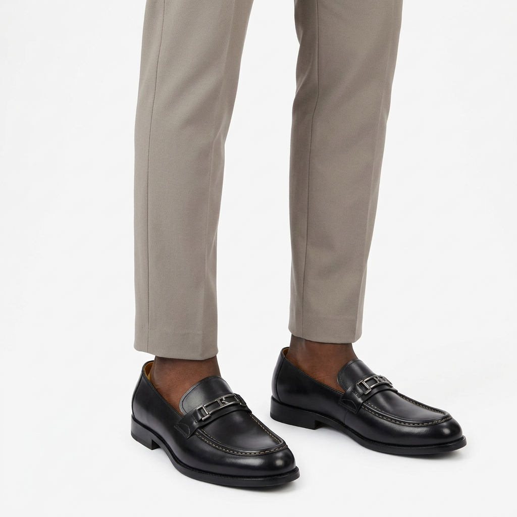Polished black loafers worn on both feet by a Black male model with tailored trousers on a white background