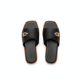 Pair of black leather wide strap flat slide slippers with gold logo hardware on white background