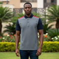 Nigerian male model wearing men's grey and navy colour-block polo shirt with red shoulder accent, garden setting