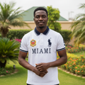 Nigerian male model wearing white graphic polo shirt with navy collar and city print in garden setting