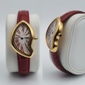 Asymmetric yellow gold watch with red Roman numerals and red strap front and side view