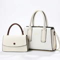 Ivory-white twin-handle handbag with dark edging beside smaller ivory flap bag with brown handle