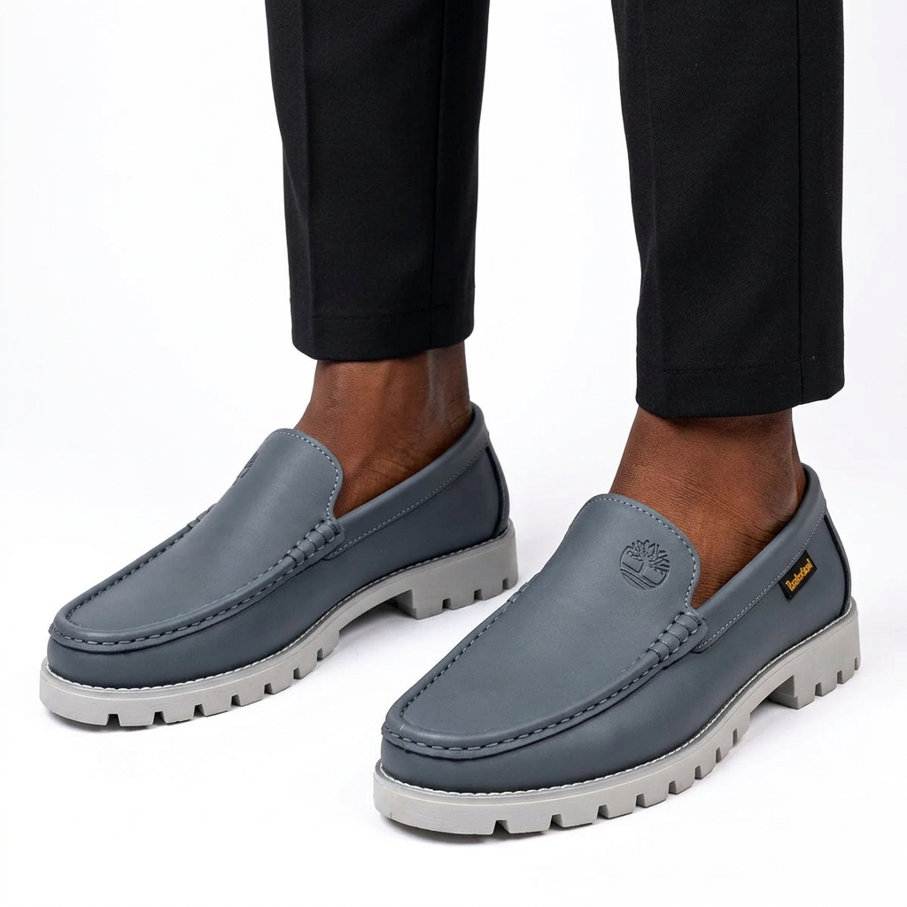 Slate grey moc-toe loafers worn on both feet by a Black male model on a white studio background