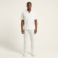 Male model wearing a white twin-pocket shirt and matching trousers against an off-white studio background