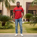 Nigerian male model wearing men's red polo shirt with navy and white chest stripe, garden setting