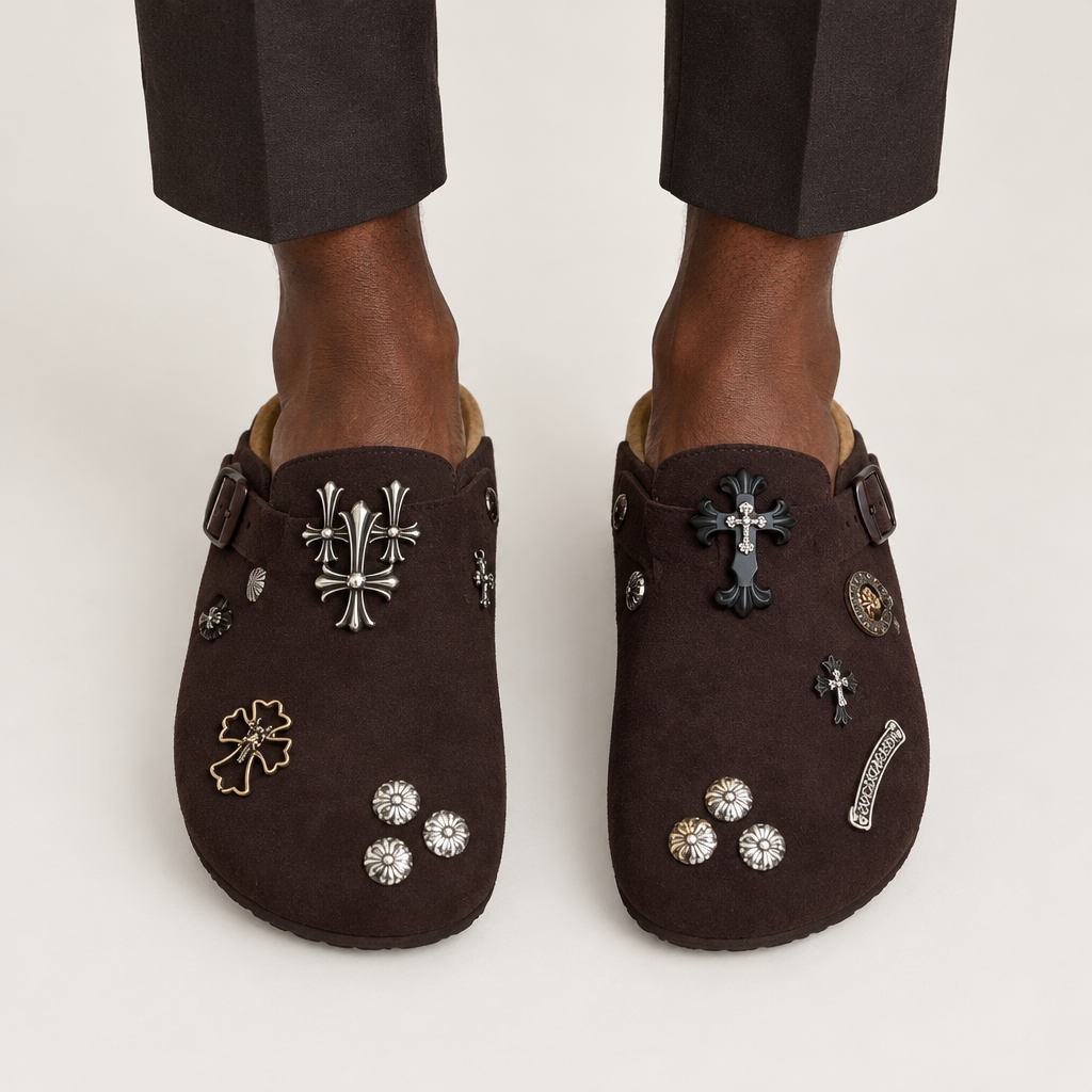 Both feet wearing chocolate cross-charm clogs on plain background