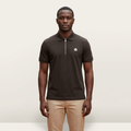Male model wearing a dark brown zip-neck polo with white chest embroidery against a plain off-white background