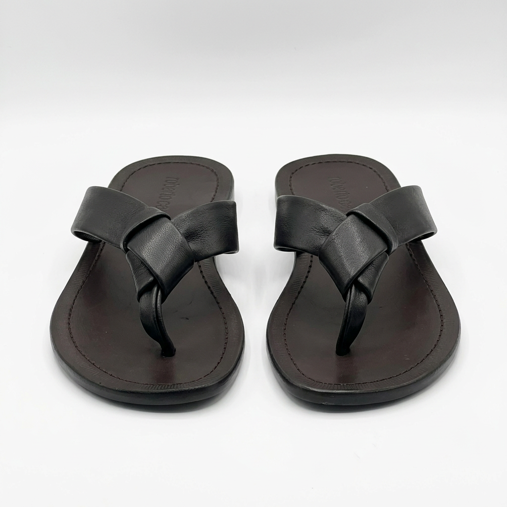 Pair of black knotted toe-post slides with brown stitched footbeds on white