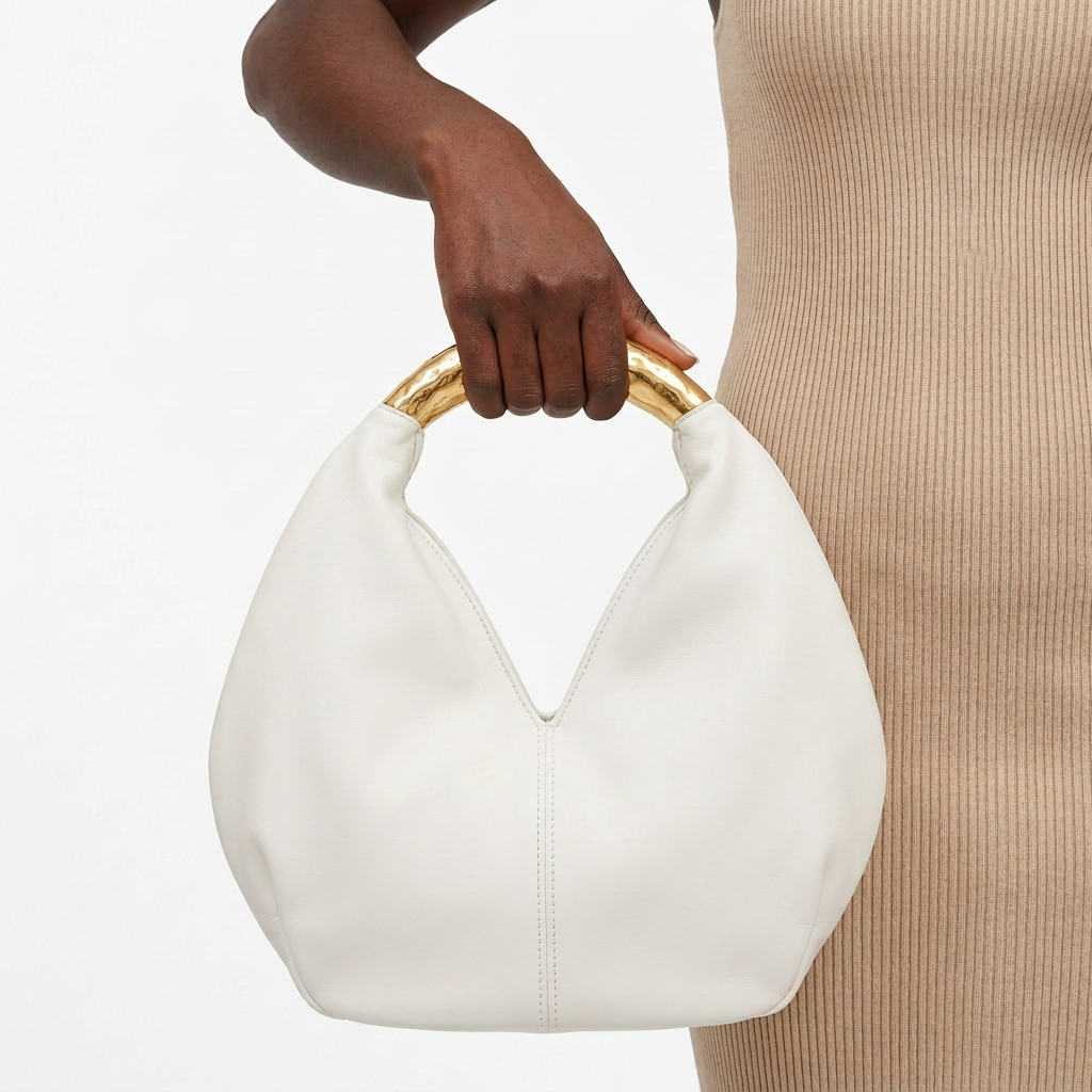 White rounded handbag without label held by one hand at its gold-tone handle