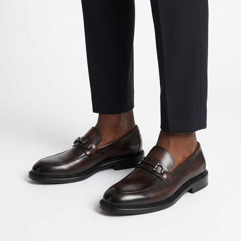 Black male model wearing both polished espresso-brown bit loafers on white