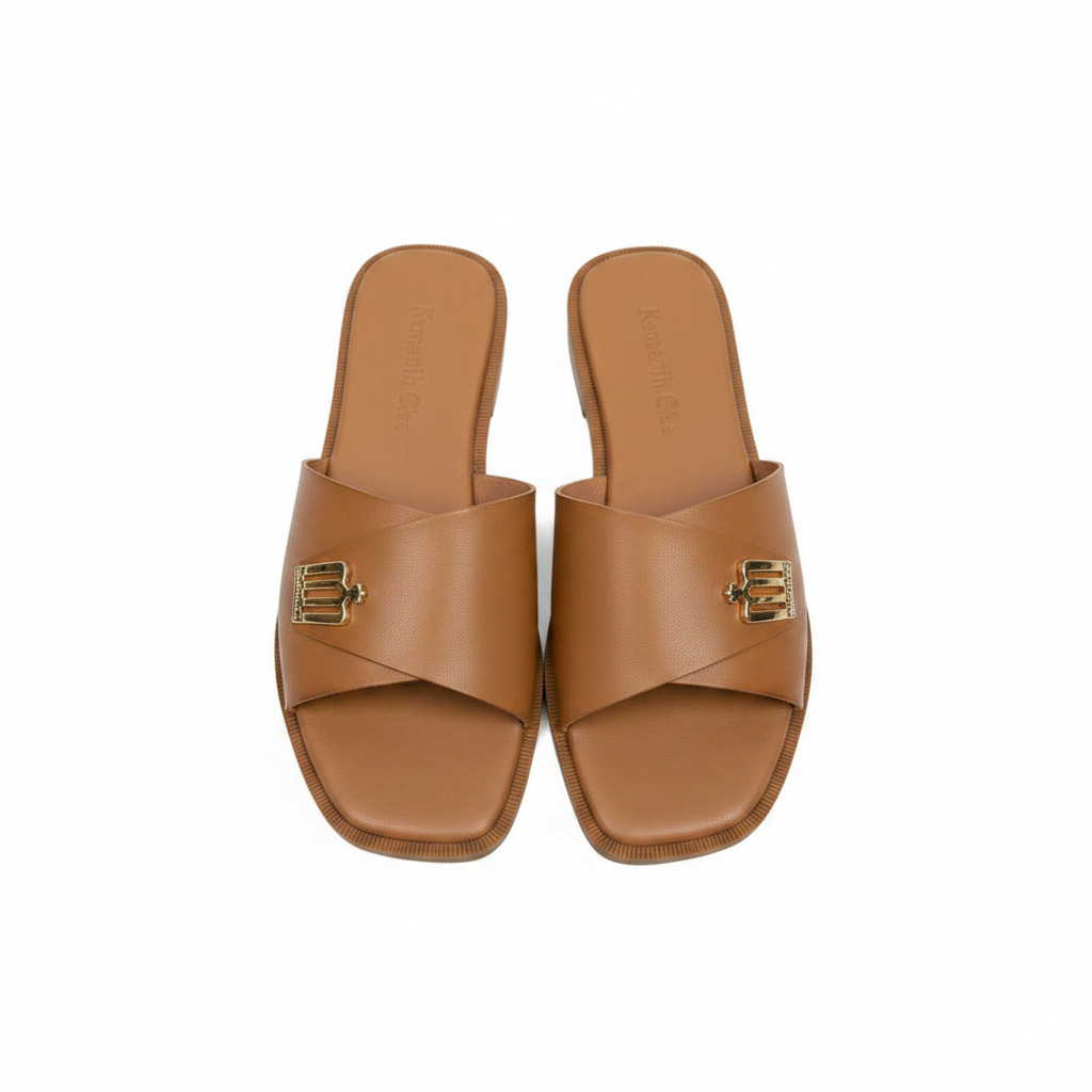 Pair of tan camel leather wide strap flat slide slippers with gold logo hardware on white background