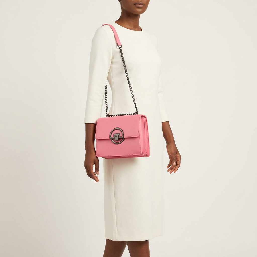 Woman in an ivory outfit wearing a pink circular-clasp chain shoulder bag against an off-white background