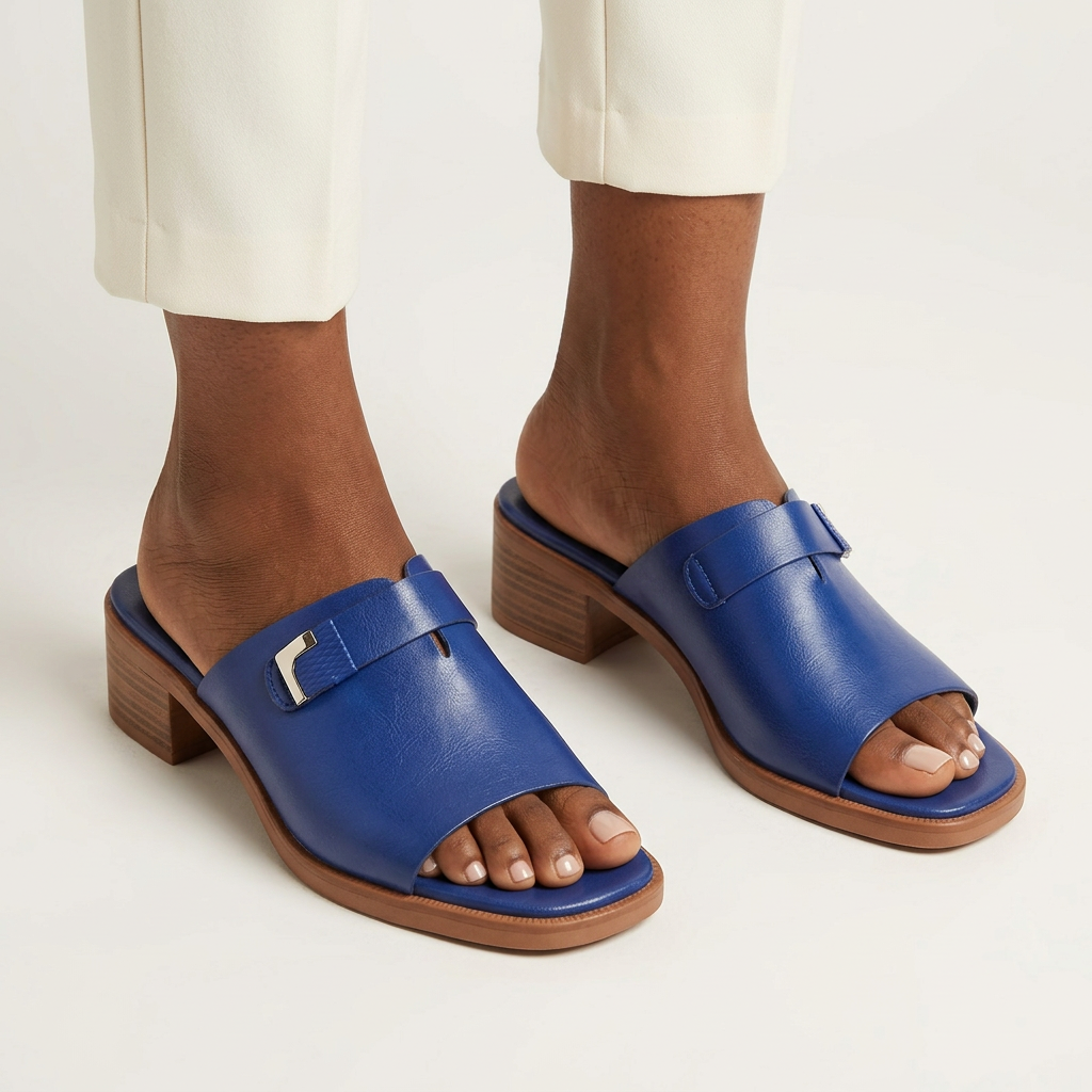 Woman wearing cobalt-blue block-heel slides with ivory trousers, both feet visible against an off-white background