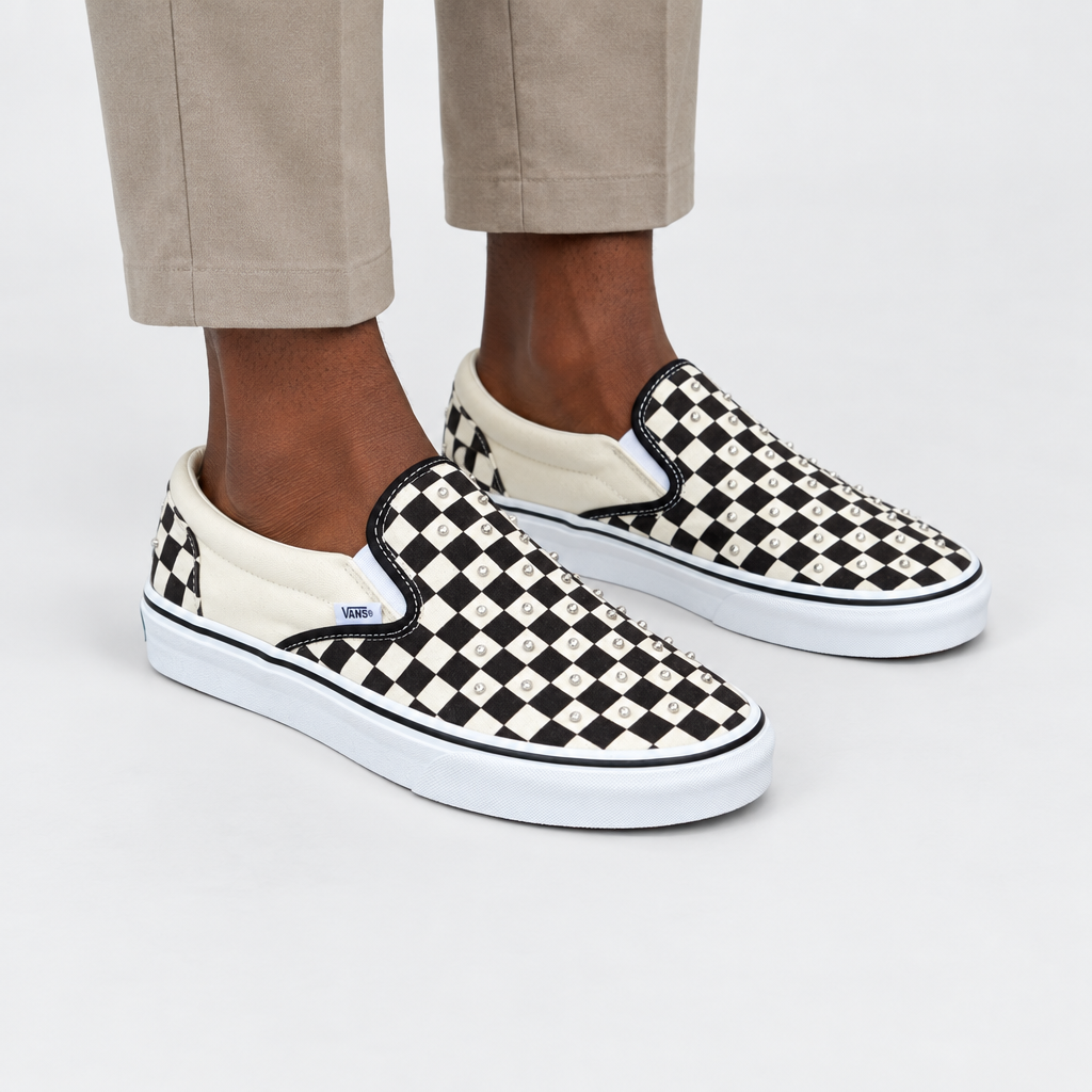 Leg-focused view of an adult wearing black-and-white studded checkerboard slip-on sneakers