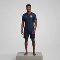 Nigerian male model full body wearing navy red away football jersey with navy shorts on concrete plinth