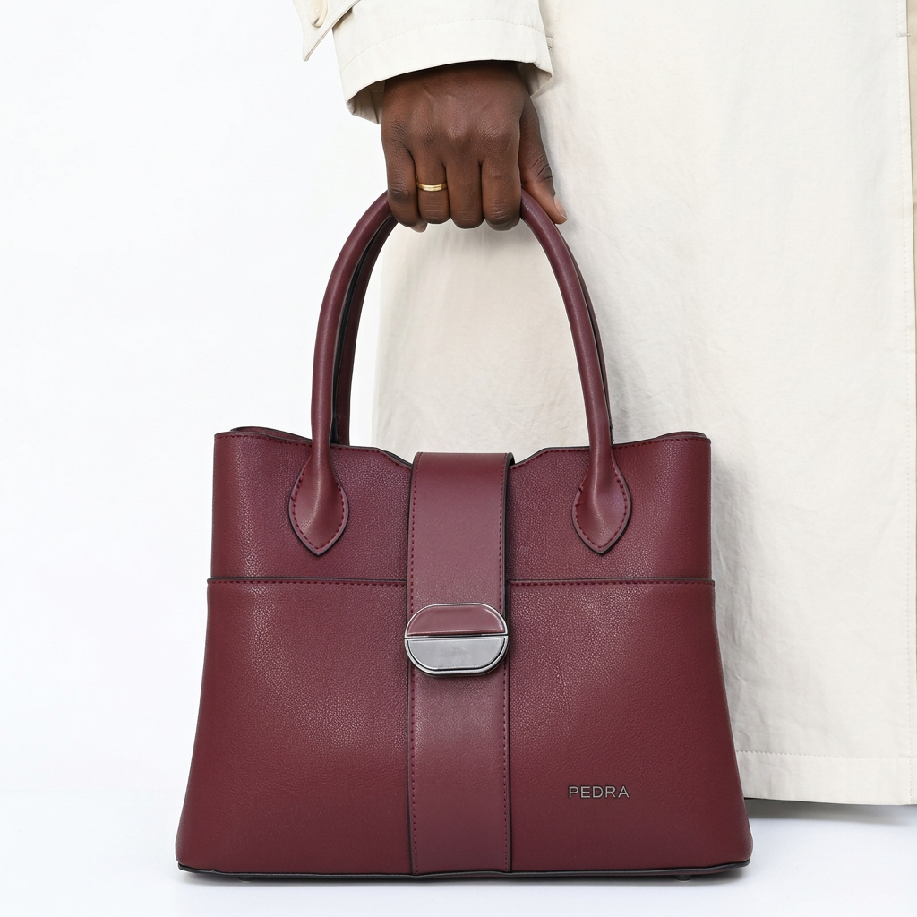 Black adult woman’s hand holding a burgundy clasp handbag on a plain white background